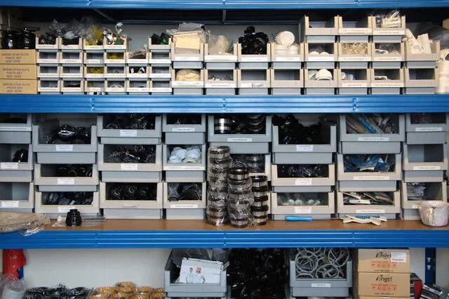 Foto des 25 m² Ersatzteillagers von slowjuicer.de, das blaue Regale mit Entsafter-Ersatzteilen wie Sieben, Schnecken, Wischblättern und mehr zeigt.