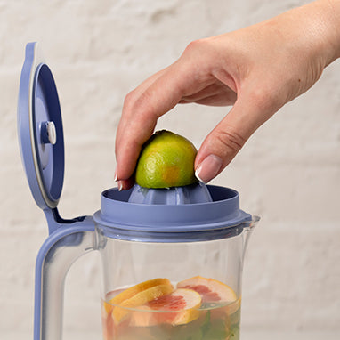 Frau presst Limette in einen 1-Liter-Vakuumbehälter mit integrierter Zitruspresse und Grapefruit-Scheiben.