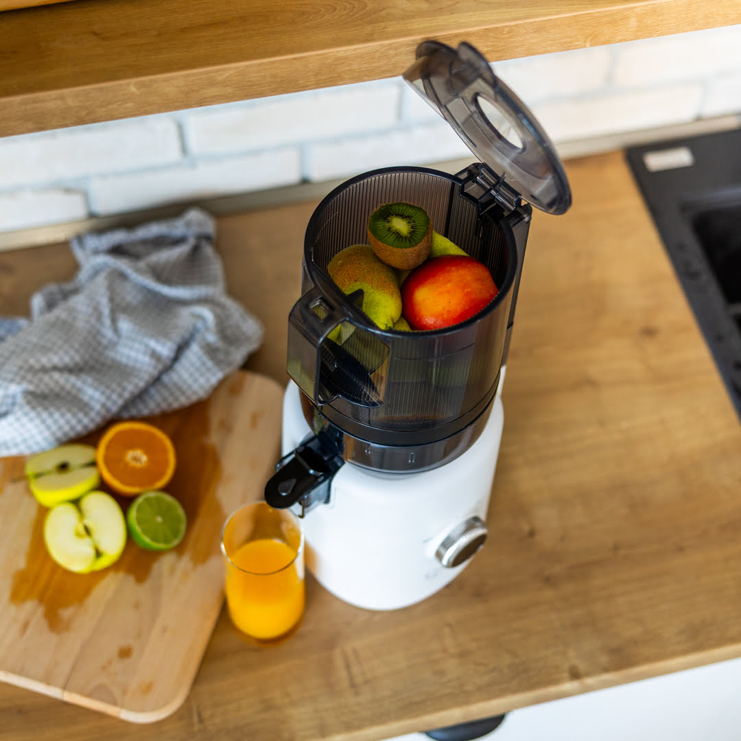 Nahaufnahme des Sana 818 Entsafters mit gefülltem Trichter, frischem Obst und Saft im Glas auf Holztheke.
