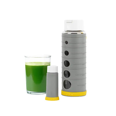 Pika Vakuumflasche aus Glas und Silikon mit einem Glas grünem Saft neben der Flasche und der Pumpe, auf weißem Hintergrund.