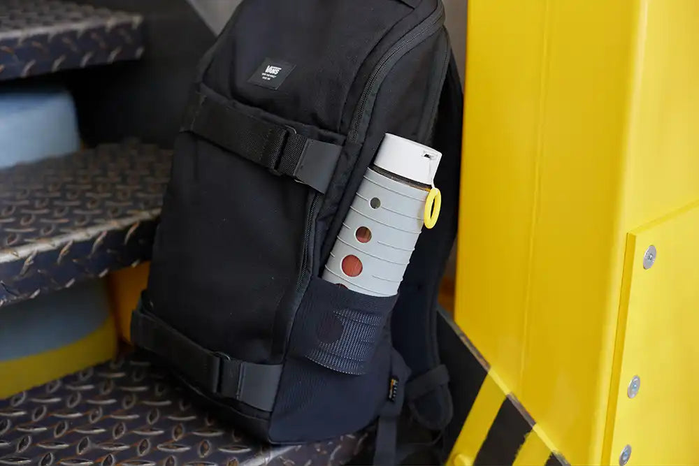 Pika Flasche mit Orangensaft gefüllt in einem Rucksack. Der Rucksack steht auf den Stufen eines Busses.